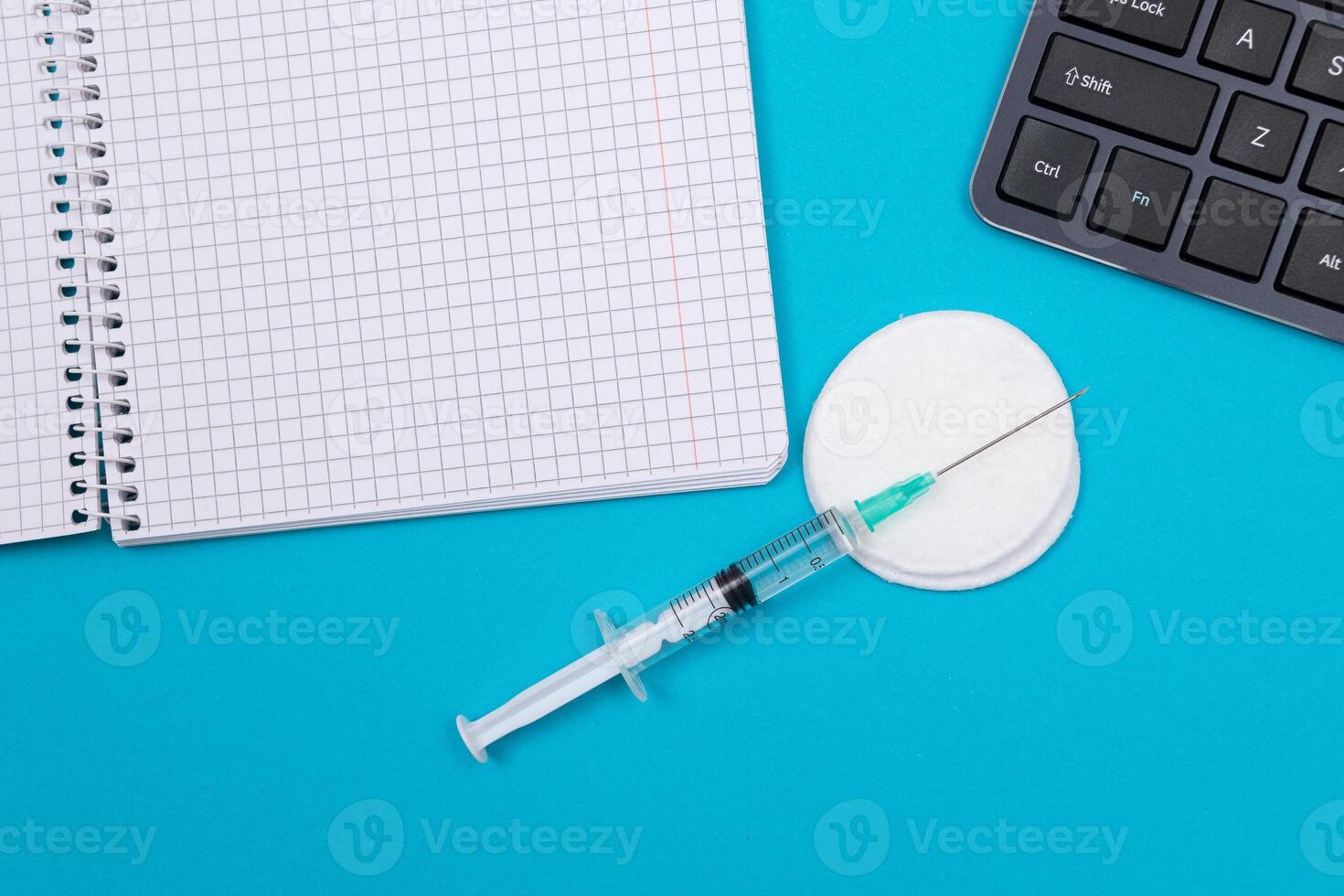 Vaccination, Immunology or Revaccination Concept - A Medical Syringe Lying on Blue Table in Doctor's Office in a Hospital or Clinic. Opened Blank Notepad - Mock Up with Copy Space photo