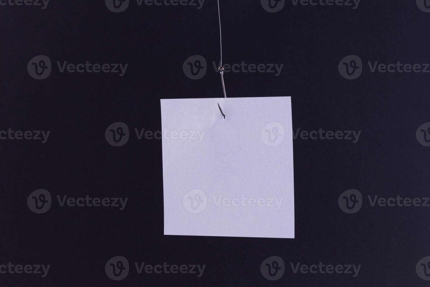 Mockup of a Blank White Memo Paper with Copy Space Hanging on a Fishing Hook Against the Black Background. Reminder or To Do List. Sticky Note Template photo