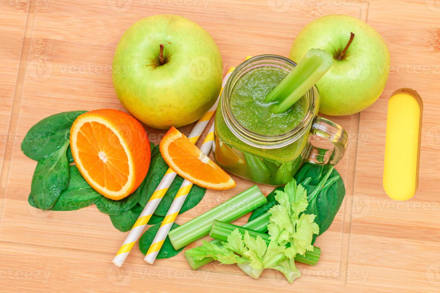 Fresh Green Smoothie of Apple, Celery, Spinach and Orange in Glass Smoothie Jar with Yellow Cocktail Straw on Wooden Cutting Board. Vegan Detox Drink. Vegetarian Culture. Healthy Eating and Fruit Diet photo