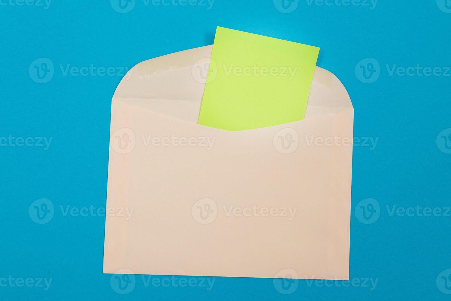 Beige Envelope with Blank Green Sheet of Paper Inside, Lying on Blue Background - Mock Up with Copy Space. Receiving Mail or Notice, Sending Postcard - Top View, Flat Lay photo