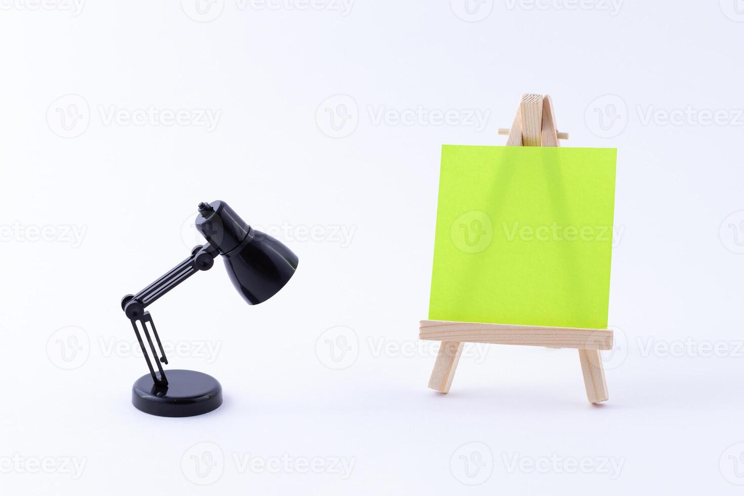 Wooden Easel Miniature with Blank Colored Square Canvas or Memo Paper - Mockup. Mini Wooden Stand with Clean Artboard and Small Black Table Lamp on White Background, Copy Space photo