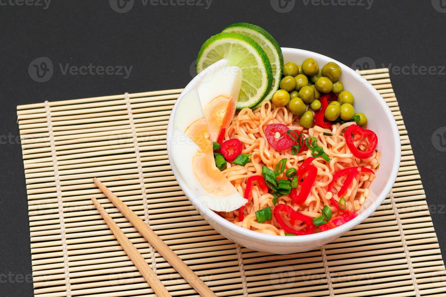 Beautiful Noodle Dish with Green Pea, Eggs, Red Hot Pepper, Greens and Lime with Chopsticks on Sushi Mat. Instant Noodles photo