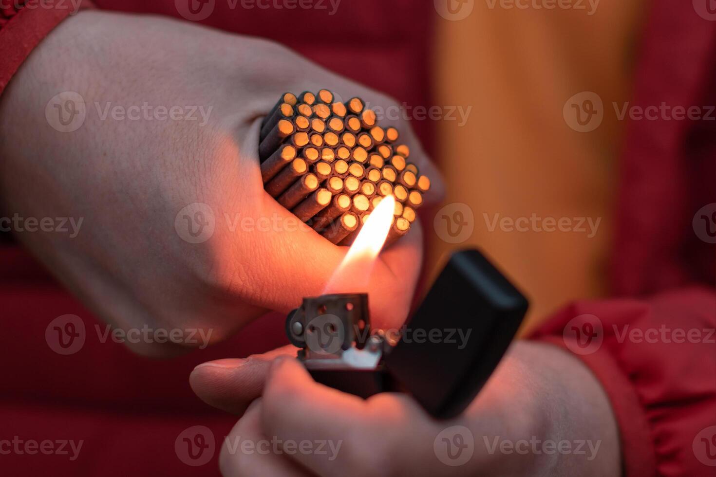Man in Red Jacked Lighting Up Many Small Black Firecrackers in his Hand Using Gasoline Lighter. Guy Getting Ready for New Year Fun with Fireworks or Pyrotechnic Products photo