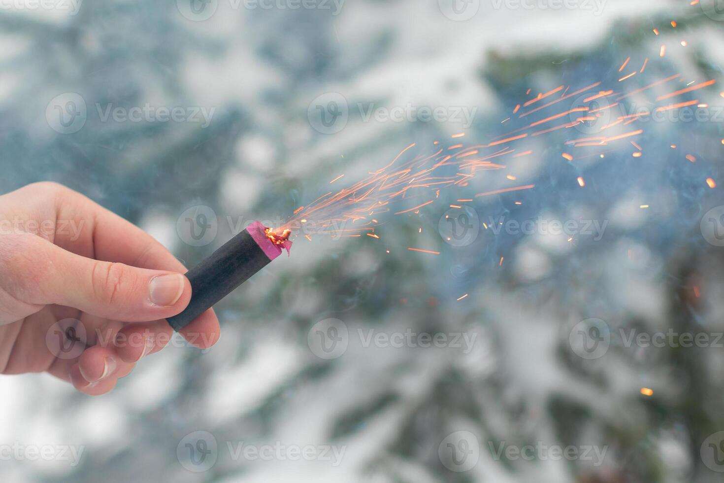 Burning Firecracker in a Hand. Guy Holding a Petard Outdoors in Winter at Daytime. Loud and Dangerous New Year's Entertainment. Hooliganism with Pyrotechnics. Noise of Firecrackers in Public Places photo