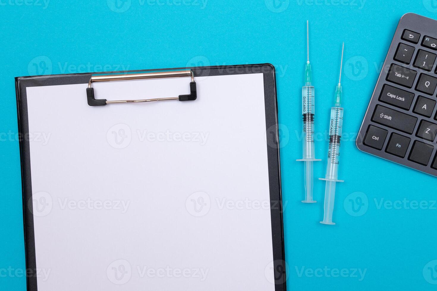 Vaccination, Immunology or Revaccination Concept - Two Medical Syringe Lying on Blue Table in Doctor's Office in a Hospital or Clinic. Black Clipboard with Sheet of Paper - Mock Up with Copy Space photo