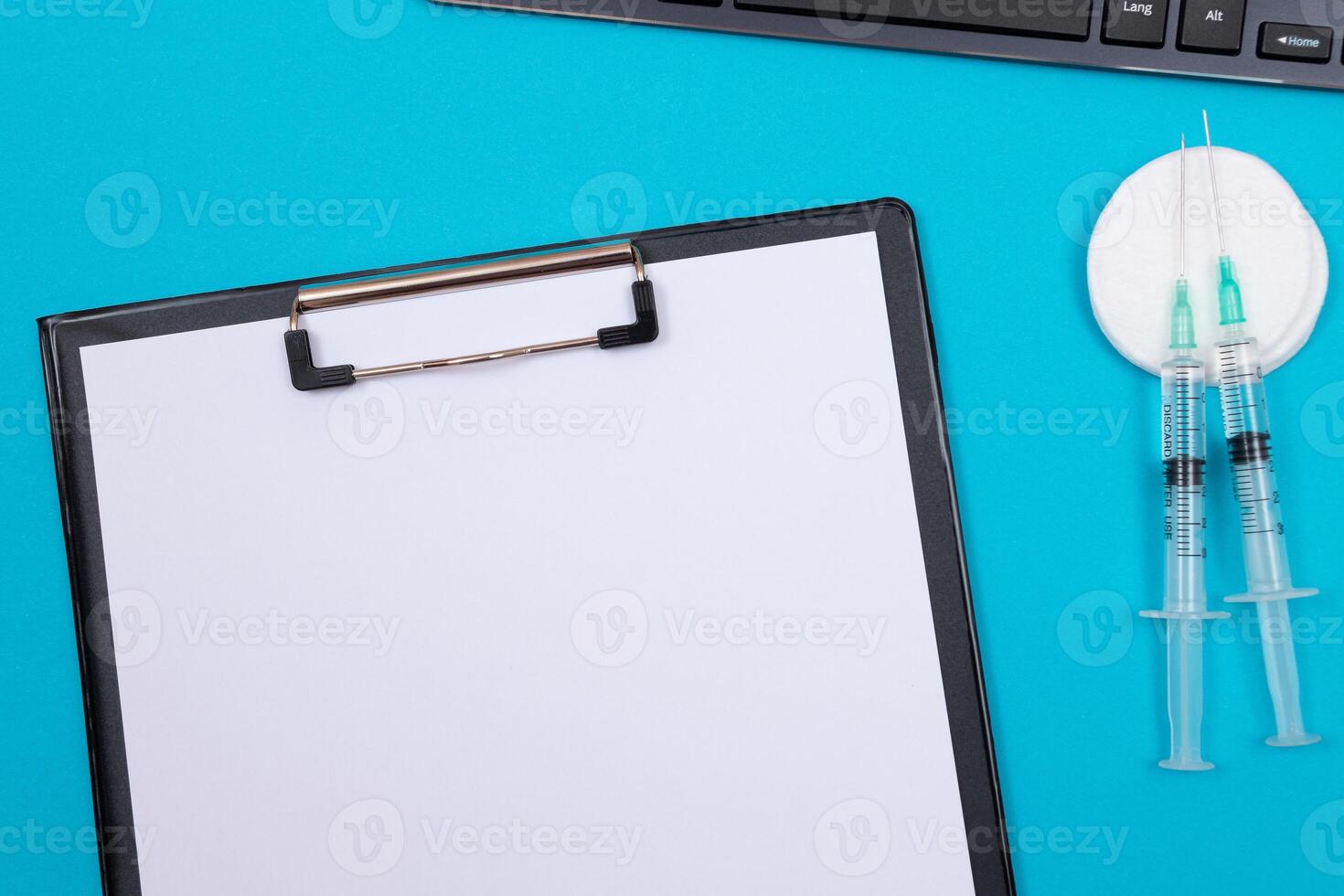 Vaccination, Immunology or Revaccination Concept - Two Medical Syringe Lying on Blue Table in Doctor's Office in a Hospital or Clinic. Black Clipboard with Sheet of Paper - Mock Up with Copy Space photo
