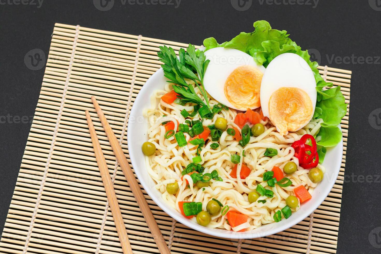 Beautiful Noodle Dish with Green Pea, Carrot, Eggs, Red Hot Pepper and Greens on Sushi Mat. Instant Noodles with Vegetables photo