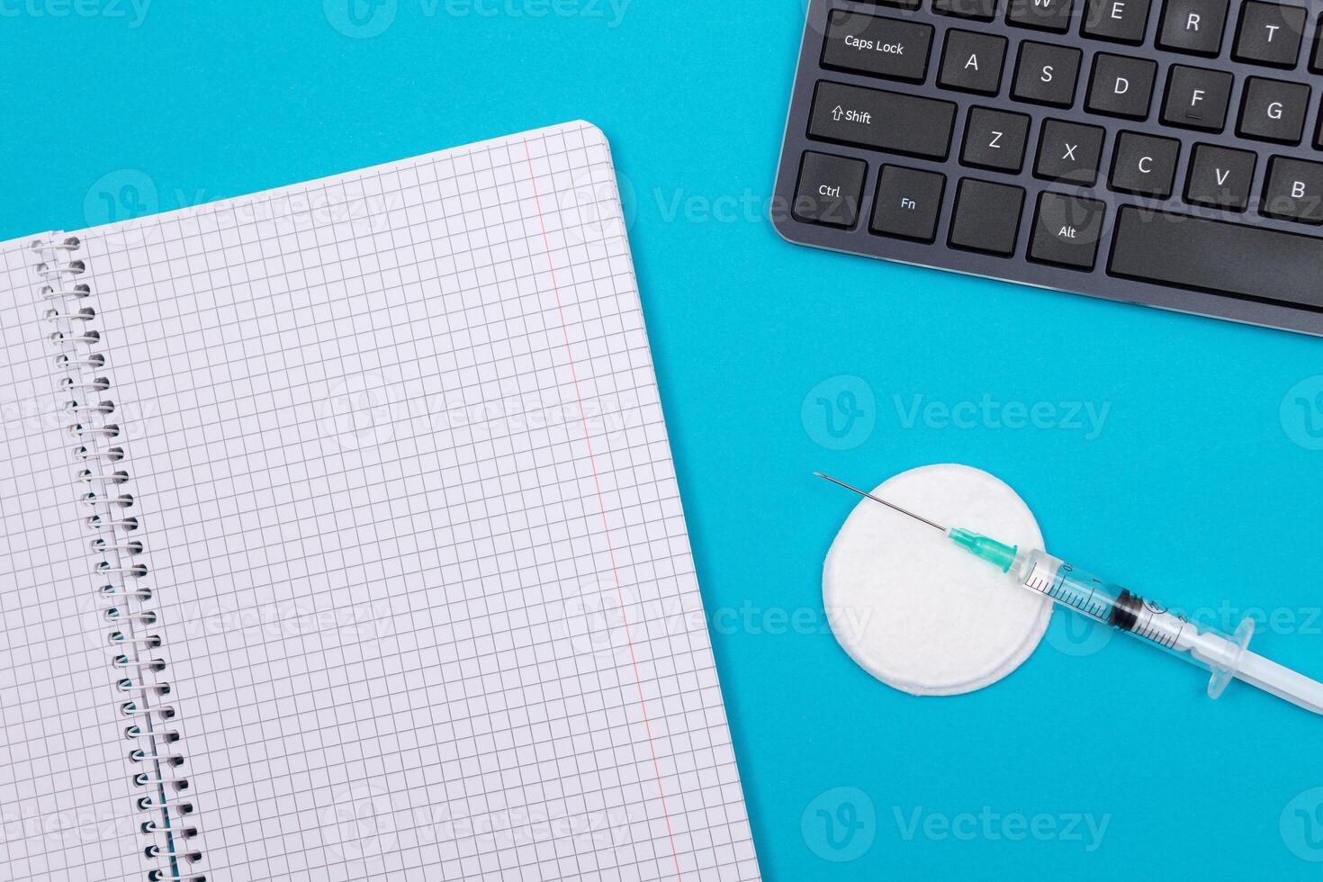 Vaccination, Immunology or Revaccination Concept - A Medical Syringe Lying on Blue Table in Doctor's Office in a Hospital or Clinic. Opened Blank Notepad - Mock Up with Copy Space photo
