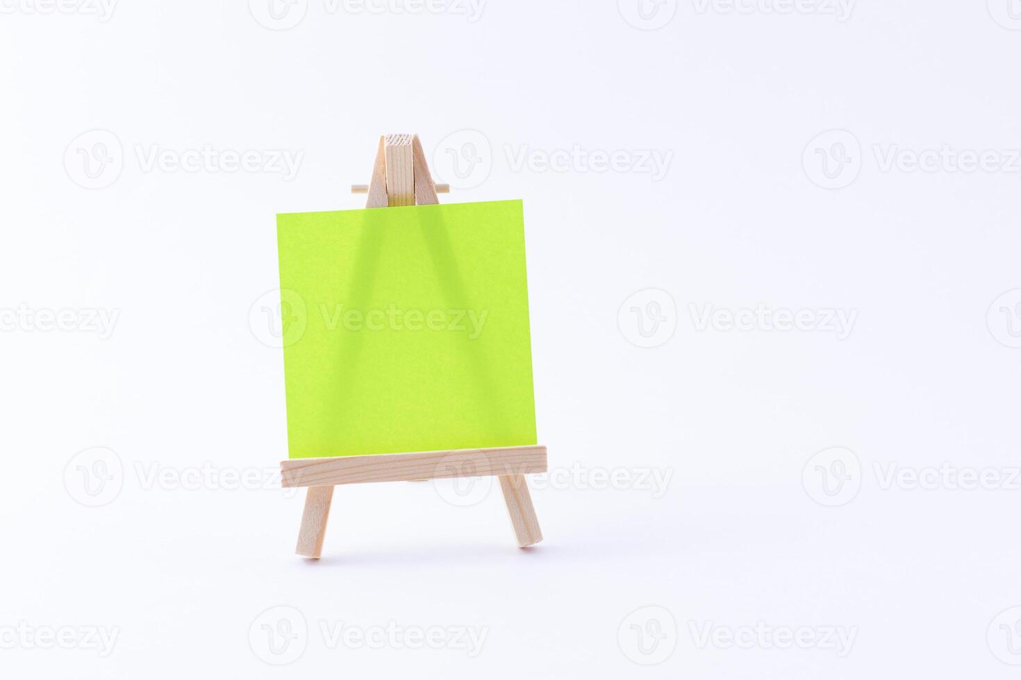 Wooden Easel Miniature with Blank Colored Square Canvas or Memo Paper - Mockup. Mini Wooden Stand with Clean Artboard on White Background, Copy Space photo