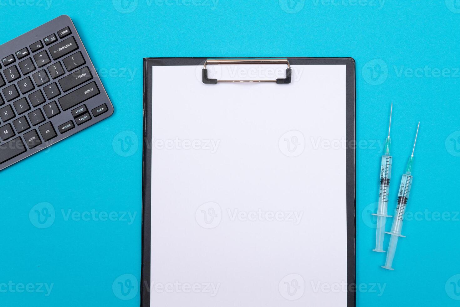 Vaccination, Immunology or Revaccination Concept - Two Medical Syringe Lying on Blue Table in Doctor's Office in a Hospital or Clinic. Black Clipboard with Sheet of Paper - Mock Up with Copy Space photo