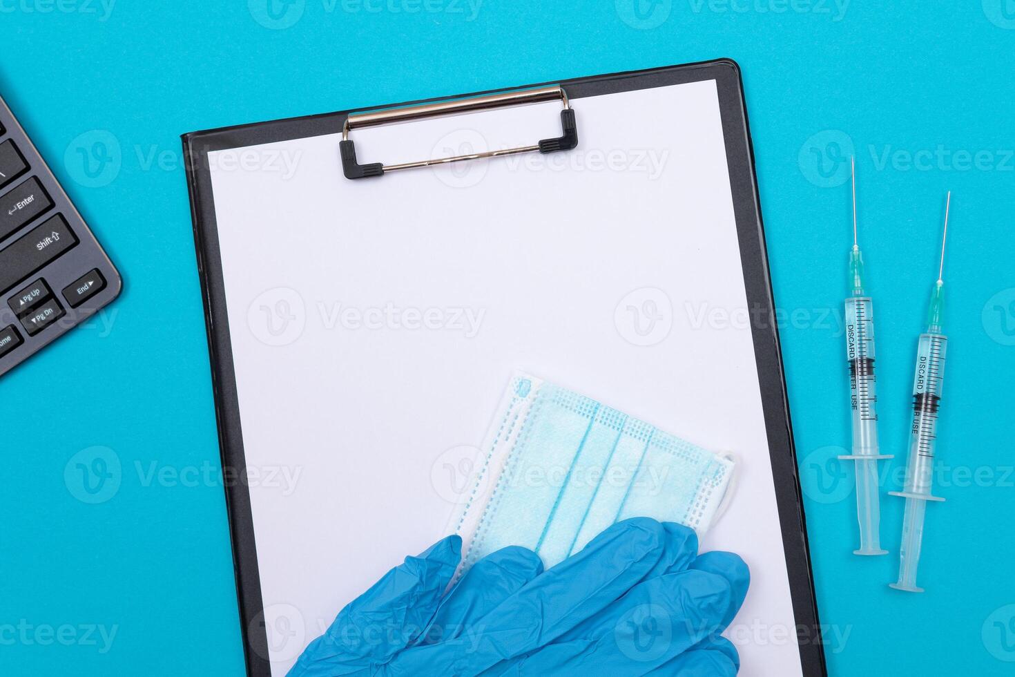 Vaccination, Immunology or Revaccination Concept - Two Medical Syringe Lying on Blue Table in Doctor's Office in a Hospital or Clinic. Black Clipboard with Sheet of Paper - Mock Up with Copy Space photo