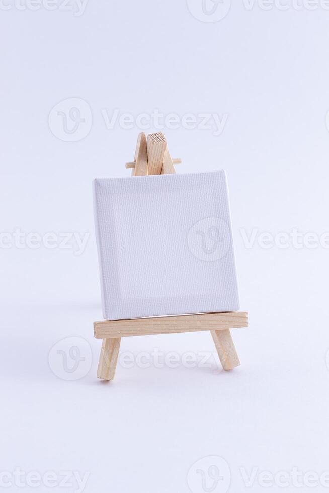 Wooden Easel Miniature with Blank White Square Canvas for Artists and Painters - Mockup. Mini Wooden Stand with Clean Artboard on White Background, Copy Space photo
