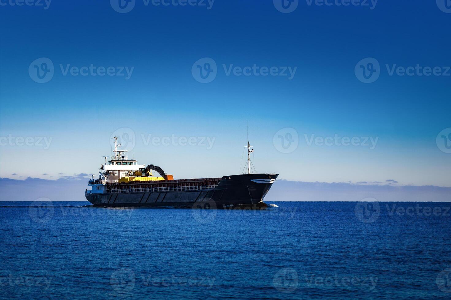 Black Sailing Bulk Carrier. Cargo Ship with Long Reach Excavator Moving in Still Water at Sunny Day by the Sea photo