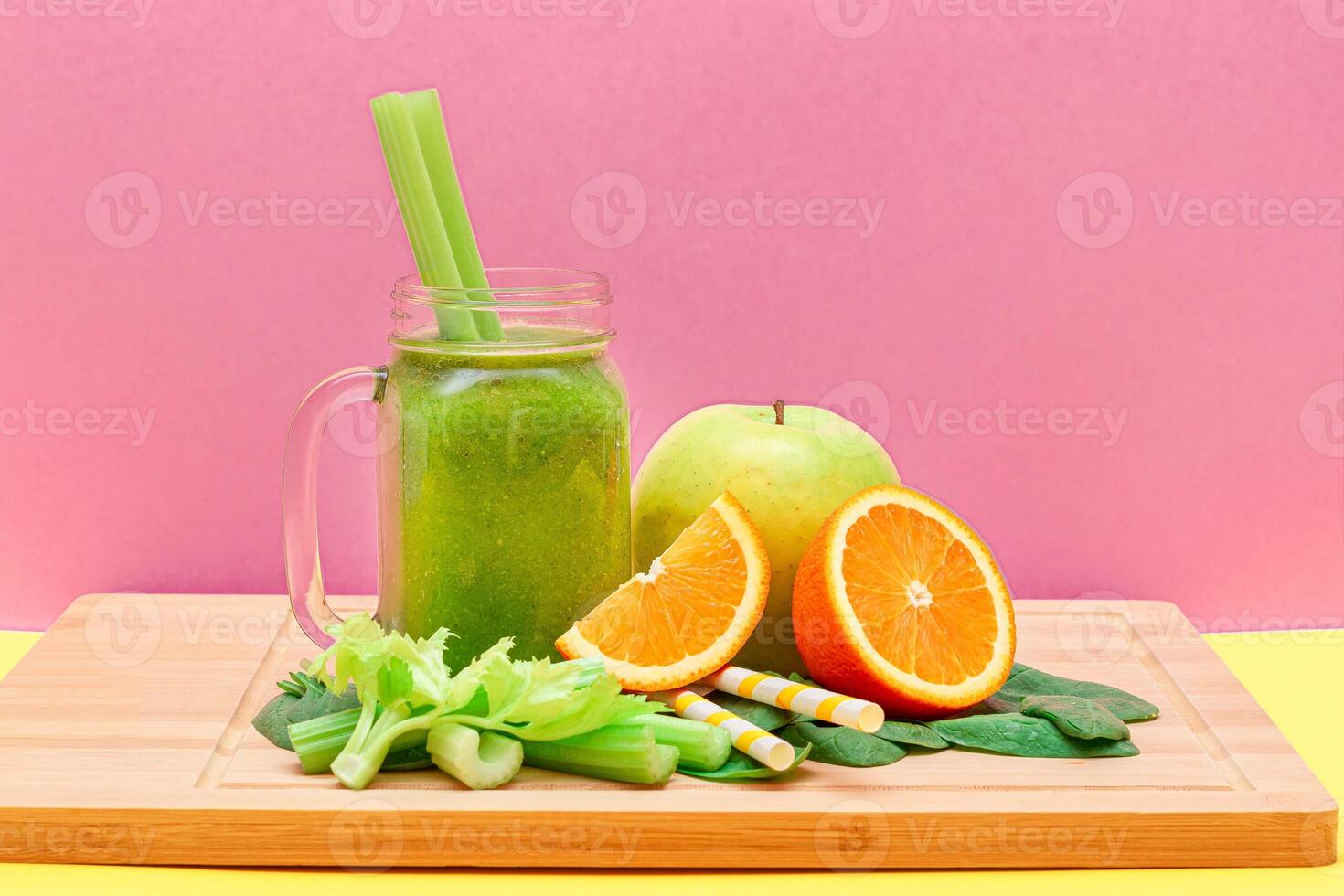 Fresh Green Smoothie of Apple, Celery, Spinach and Orange in Glass Smoothie Jar with Yellow Cocktail Straw on Wooden Cutting Board. Vegan Detox Drink. Vegetarian Culture. Healthy Eating and Fruit Diet photo