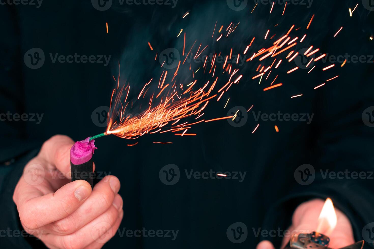 The Firecracker in a Hand. Man Holding a Burning Petard in His Hand. A Human with a Pyrotechnics that Burns with Sparks and Smoke Outdoors photo