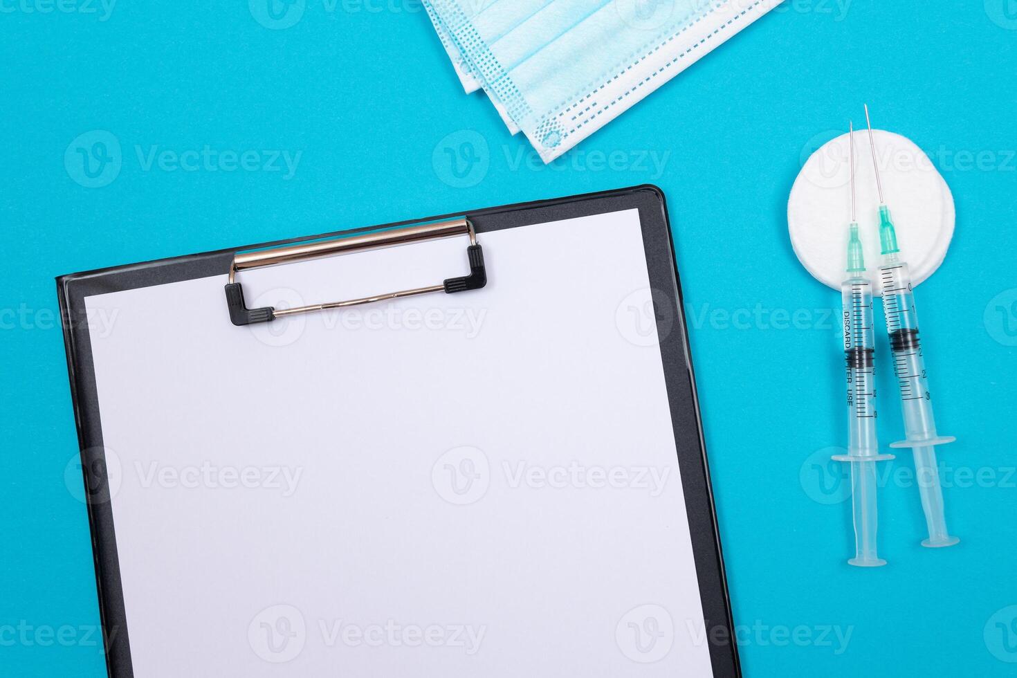 Vaccination, Immunology or Revaccination Concept - Two Medical Syringe Lying on Blue Table in Doctor's Office in a Hospital or Clinic. Black Clipboard with Sheet of Paper - Mock Up with Copy Space photo