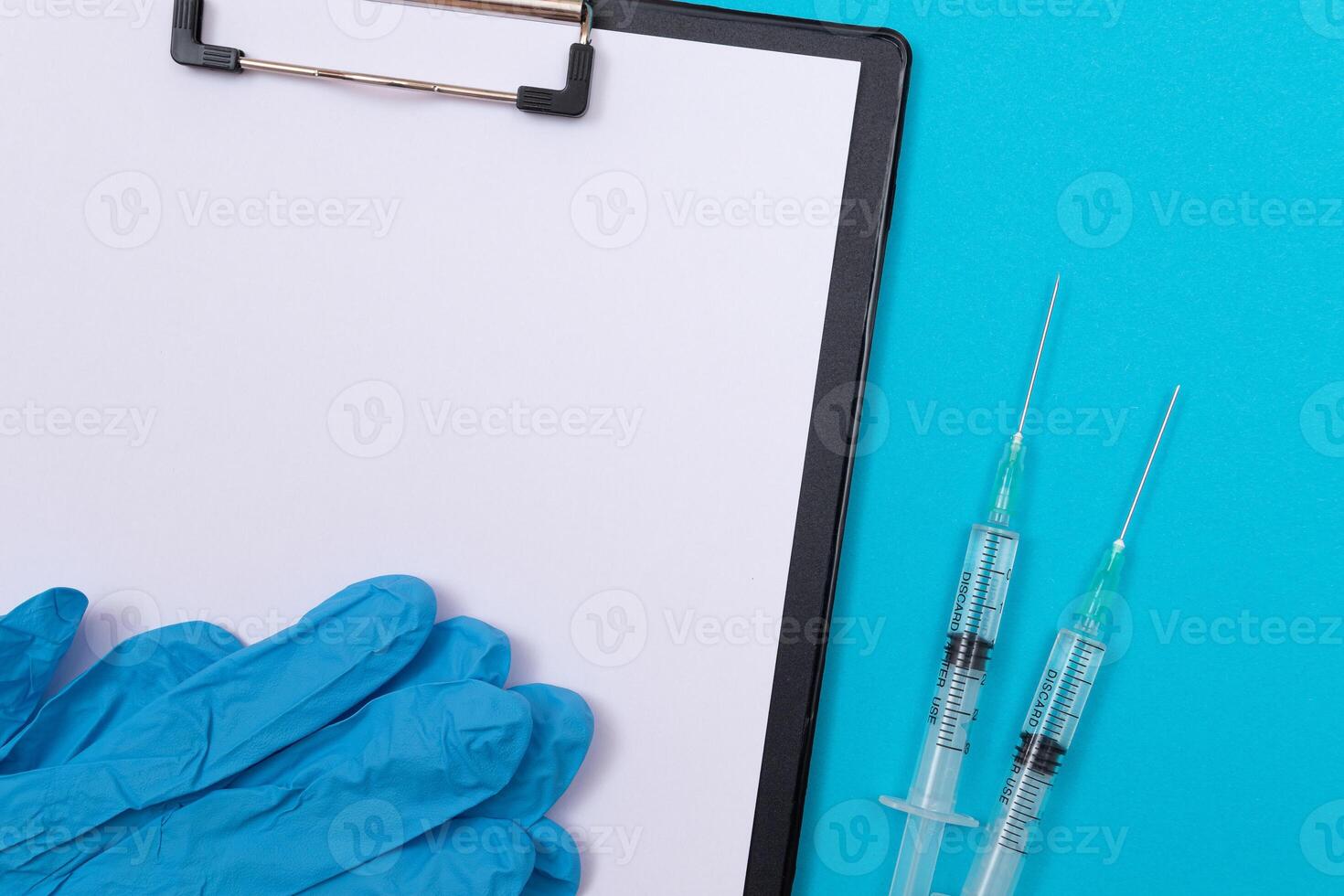 Vaccination, Immunology or Revaccination Concept - Two Medical Syringe Lying on Blue Table in Doctor's Office in a Hospital or Clinic. Black Clipboard with Sheet of Paper - Mock Up with Copy Space photo