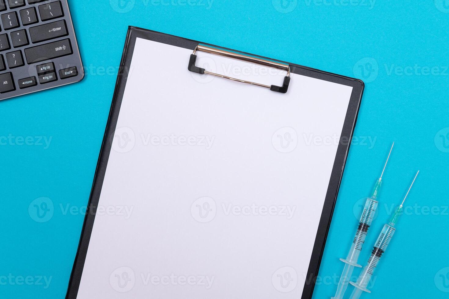 Vaccination, Immunology or Revaccination Concept - Two Medical Syringe Lying on Blue Table in Doctor's Office in a Hospital or Clinic. Black Clipboard with Sheet of Paper - Mock Up with Copy Space photo