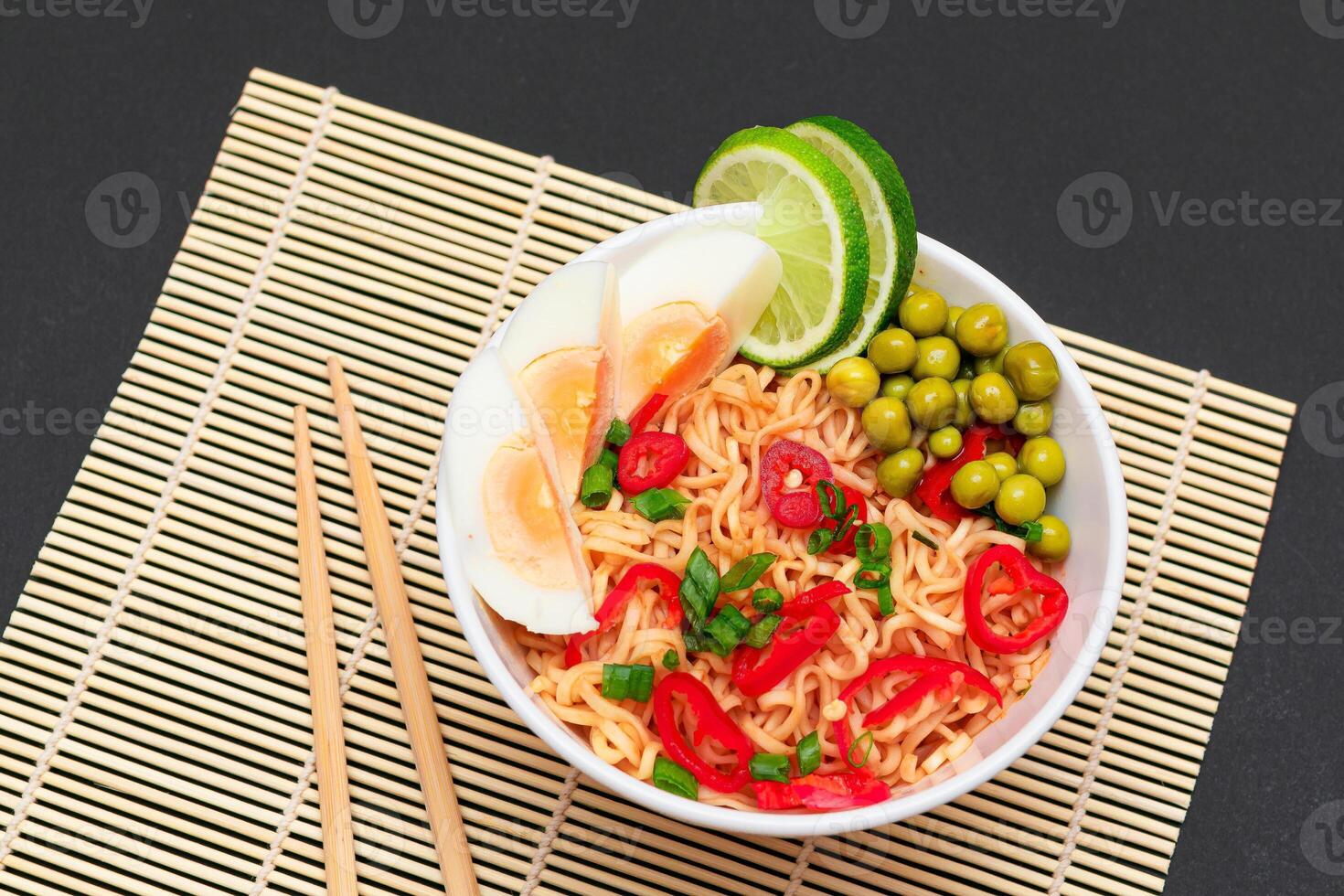 Beautiful Noodle Dish with Green Pea, Eggs, Red Hot Pepper, Greens and Lime with Chopsticks on Sushi Mat. Instant Noodles photo