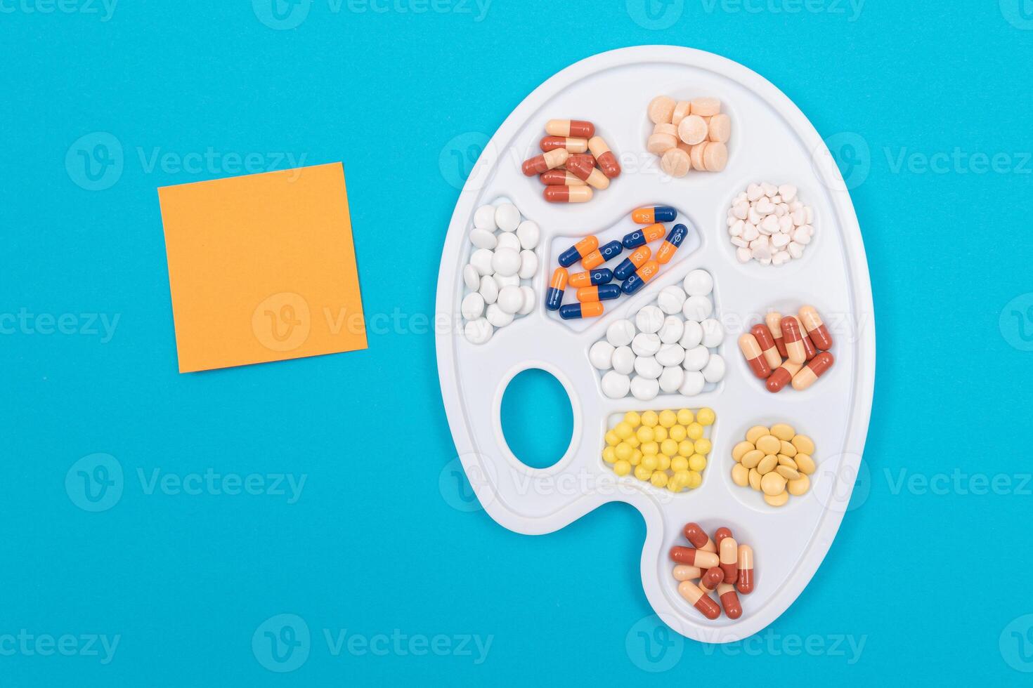 Global Pharmaceutical Industry and Medicinal Products - Different Colored Pills, Tablets and Capsules on White Art Palette with Blank Sticky Note and Copy Space Lying on Blue Background, Flat Lay photo