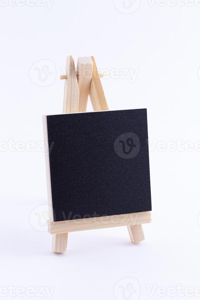 Wooden Easel Miniature with Blank Black Square Canvas for Artists and Painters - Mockup. Mini Wooden Stand with Clean Artboard on White Background, Copy Space photo
