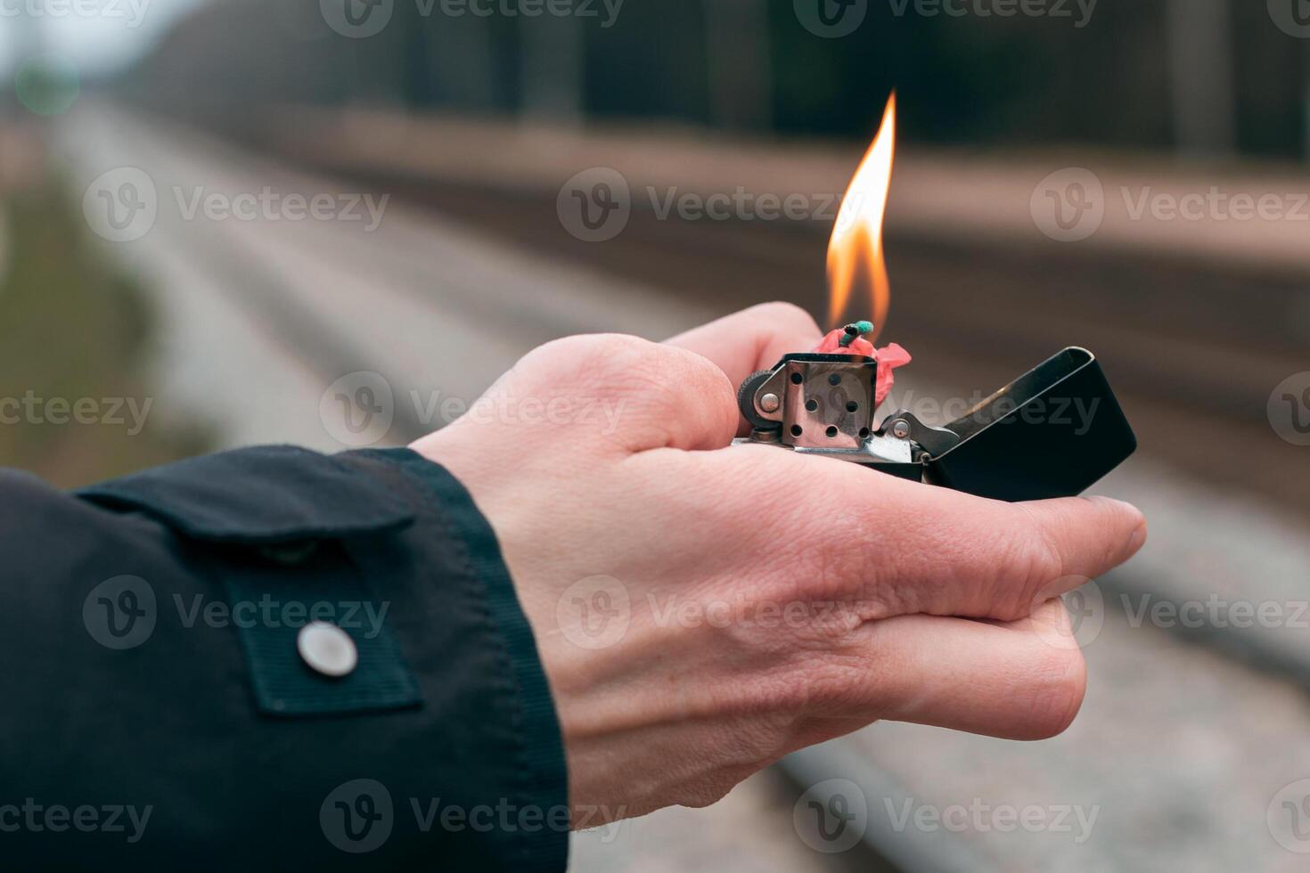 Setting Fire to the Firecracker. Man in Black Clothes Lighting Up the Petard. Firing Up the Pyrotechnics with a Black Gasoline Lighter Outdoors photo