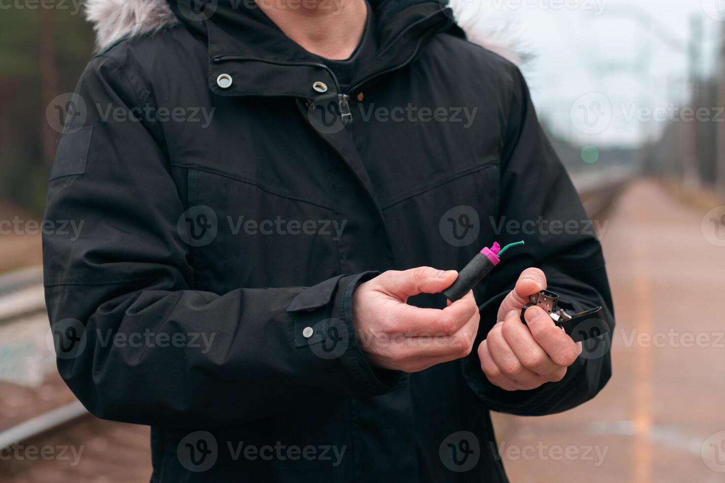 Setting Fire to the Firecracker. Man in Black Clothes Lighting Up the Petard. Firing Up the Pyrotechnics with a Black Gasoline Lighter Outdoors photo