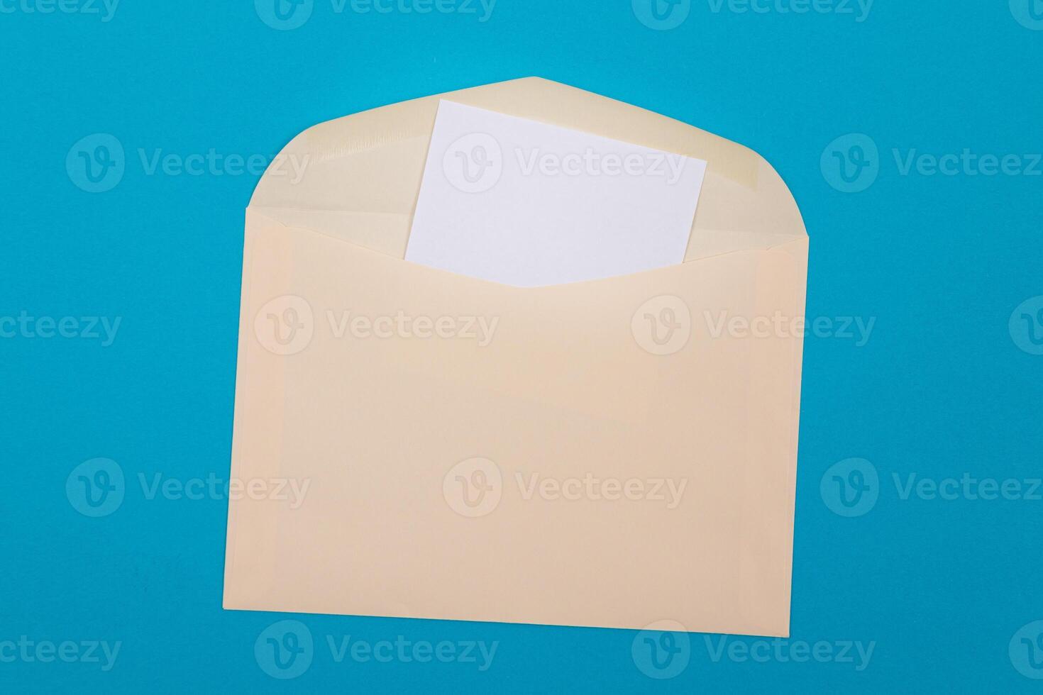 Beige Envelope with Blank White Sheet of Paper Inside, Lying on Blue Background - Mock Up with Copy Space. Receiving Mail or Notice, Sending Postcard - Top View, Flat Lay photo