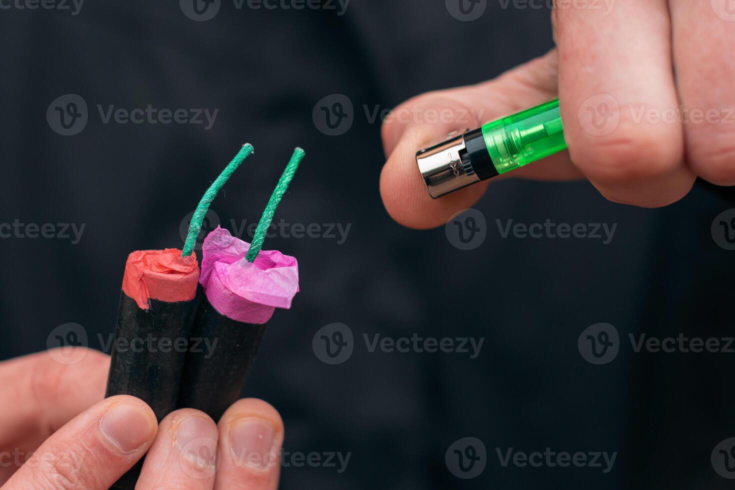 Setting Fire to the several Firecrackers. Man in Black Clothes Lighting Up Two Petards at the Same Time. Firing Up the Pyrotechnic with Green Gas Lighter Outdoors photo