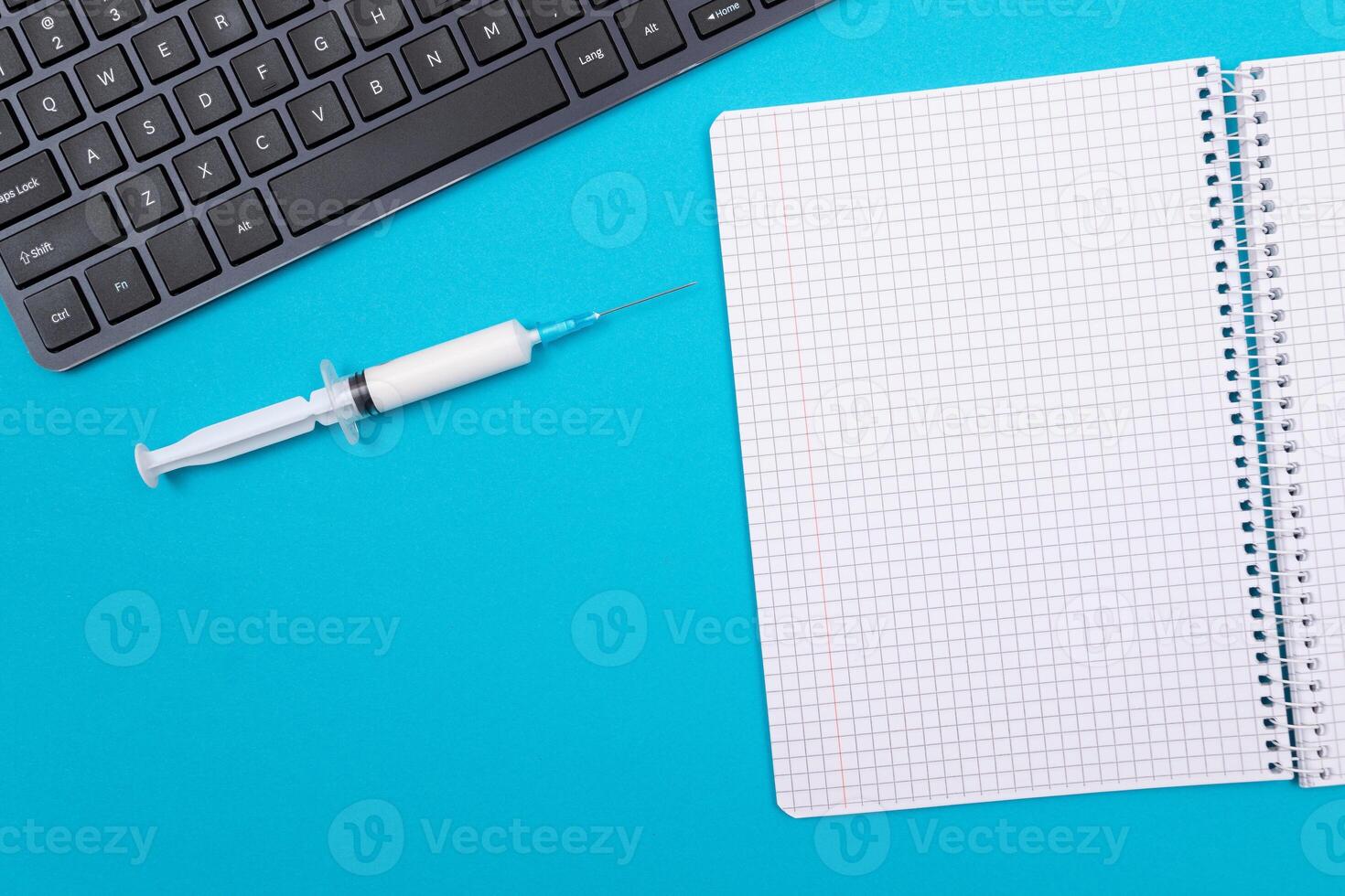 Vaccination, Immunology or Revaccination Concept - A Medical Syringe Lying on Blue Table in Doctor's Office in a Hospital or Clinic. Opened Blank Notepad - Mock Up with Copy Space photo