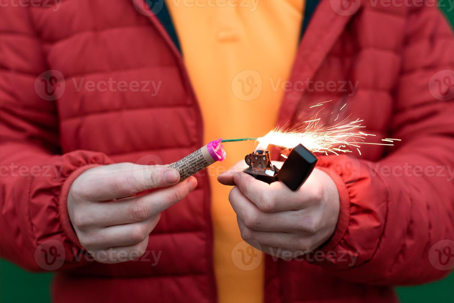 Man in Red Jacked Lighting Up Firecracker in his Hand Using Gasoline Lighter. Guy Getting Ready for New Year Fun with Fireworks or Pyrotechnic Products photo