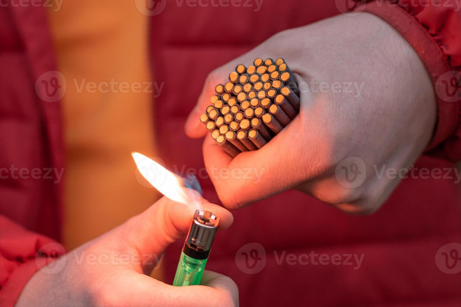 Man in Red Jacked Lighting Up Many Small Black Firecrackers in his Hand Using Gas Lighter. Guy Getting Ready for New Year Fun with Fireworks or Pyrotechnic Products photo