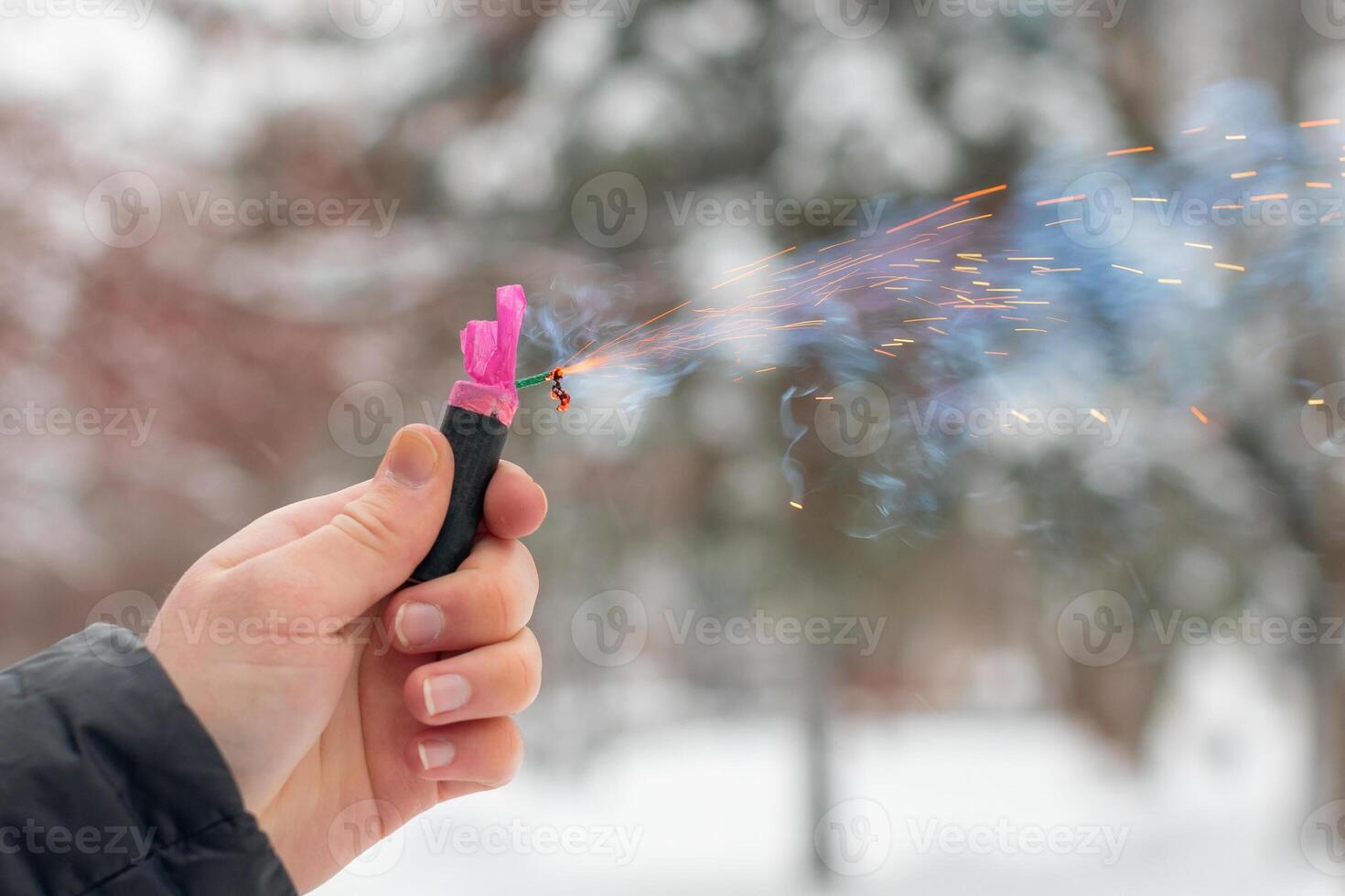 Burning Firecracker in a Hand. Guy Holding a Petard Outdoors in Winter at Daytime. Loud and Dangerous New Year's Entertainment. Hooliganism with Pyrotechnics. Noise of Firecrackers in Public Places photo