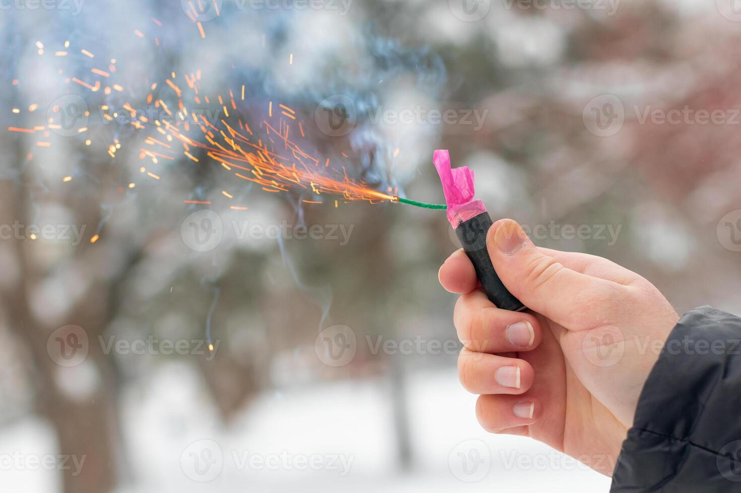 Burning Firecracker in a Hand. Guy Holding a Petard Outdoors in Winter at Daytime. Loud and Dangerous New Year's Entertainment. Hooliganism with Pyrotechnics. Noise of Firecrackers in Public Places photo