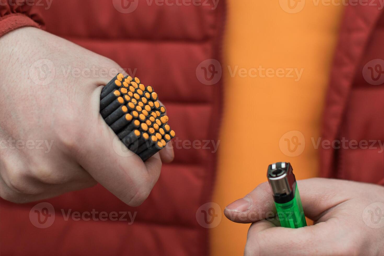 Man in Red Jacked Lighting Up Many Small Black Firecrackers in his Hand Using Gas Lighter. Guy Getting Ready for New Year Fun with Fireworks or Pyrotechnic Products photo