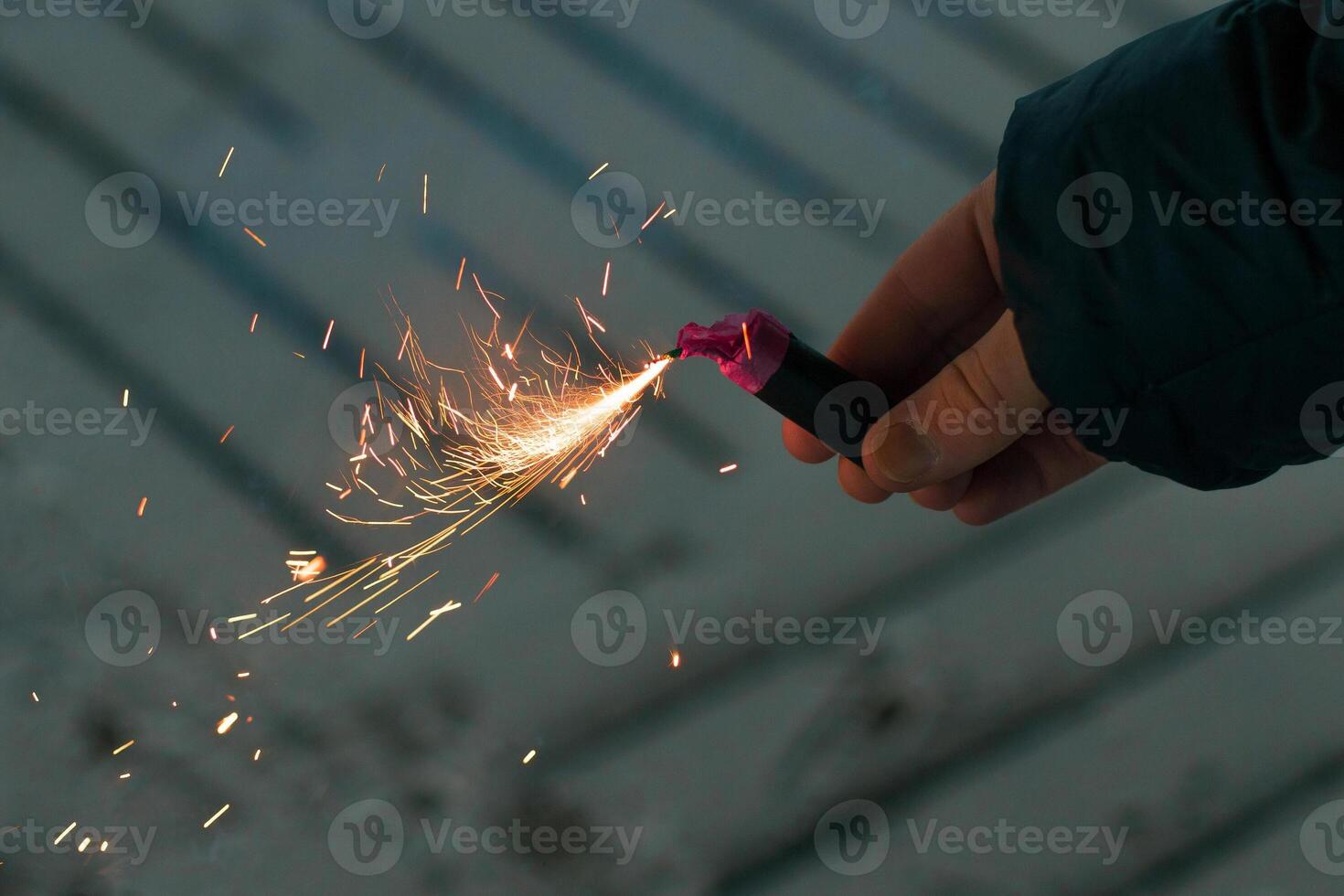 Burning Firecracker with Sparks. Guy Holding a Petard in a Hand. Loud and Dangerous New Year's Entertainment. Hooliganism with Pyrotechnics. Noise of Firecrackers in Public Places photo