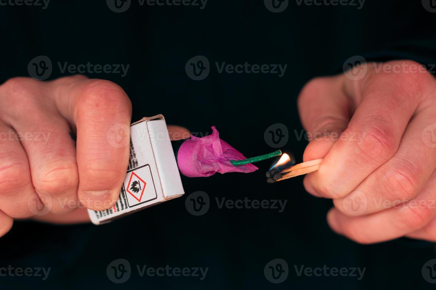 Setting Fire to the Firecracker. Man in Black Clothes Lighting Up the Petard. Pyrotechnics Firing Up with Matches Holding Together with a Matchbox Outdoors photo