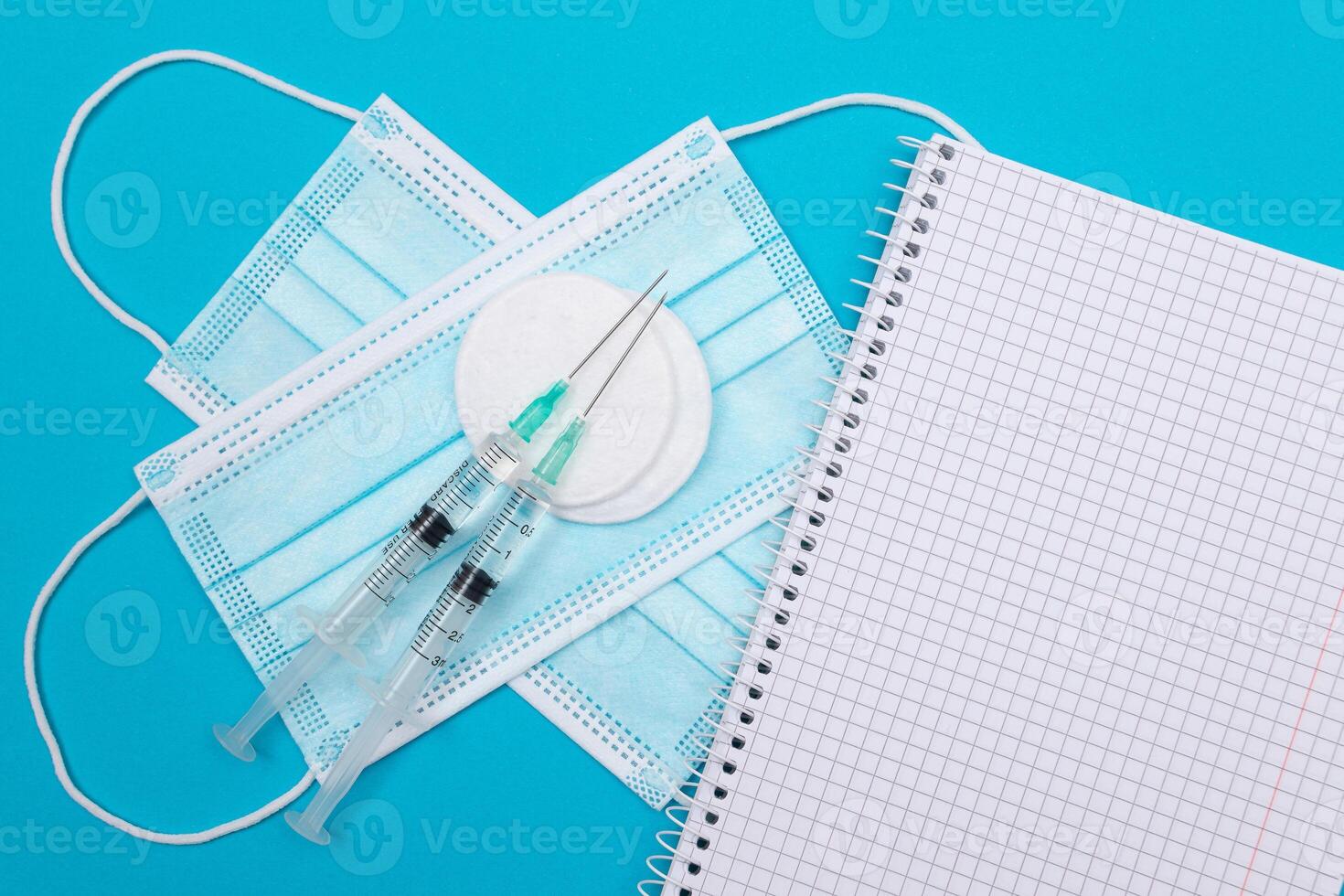 Vaccination, Immunology or Revaccination Concept - Two Medical Syringe Lying on Blue Table in Doctor's Office in a Hospital or Clinic. Opened Blank Notepad - Mock Up with Copy Space photo
