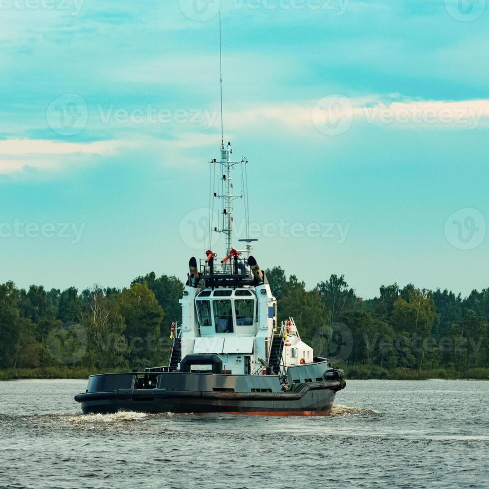 Black tug ship moving to the cargo terminal. Industrial service photo