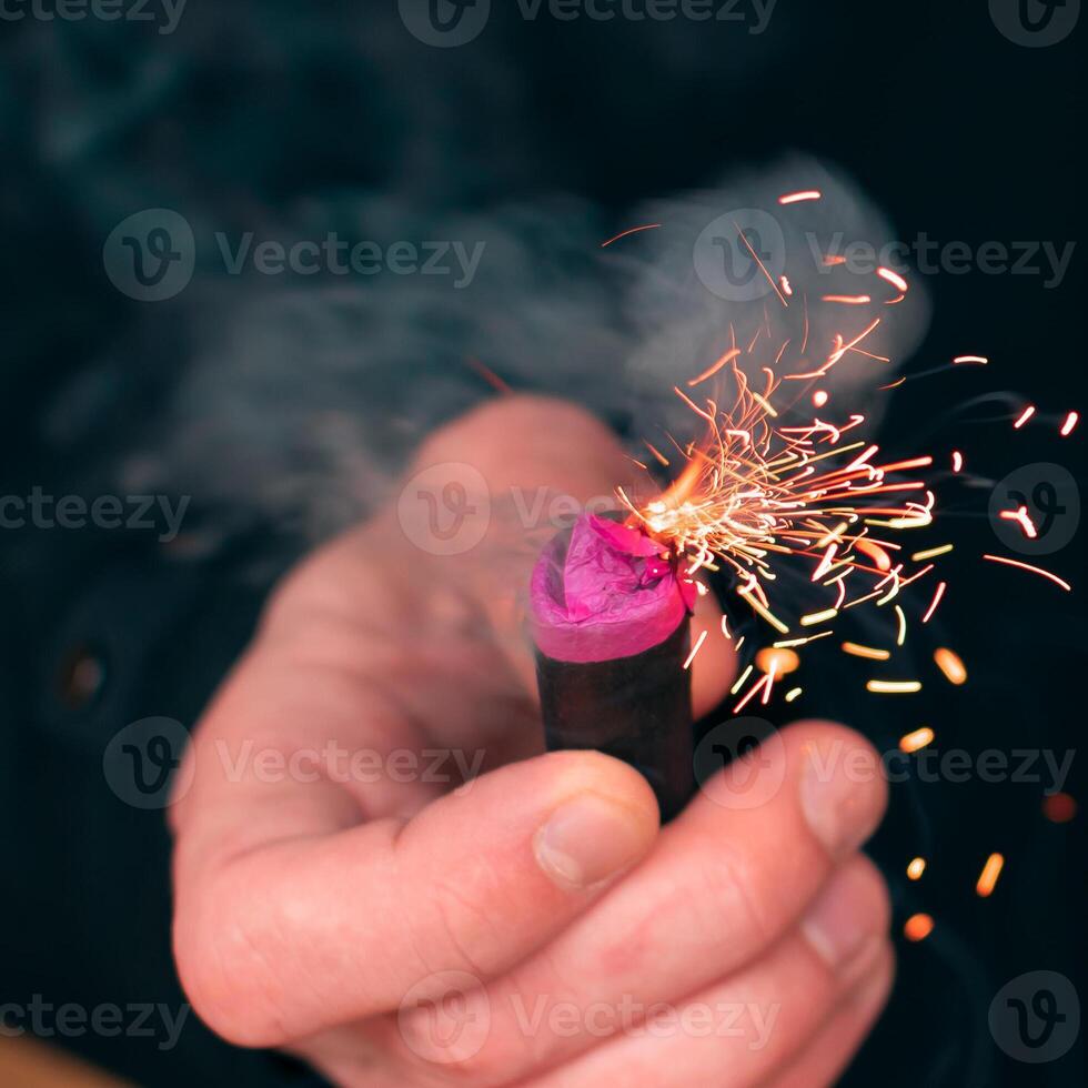 The Firecracker in a Hand. Man Holding a Burning Petard in His Hand. A Human with a Pyrotechnics that Burns with Sparks and Smoke Outdoors photo