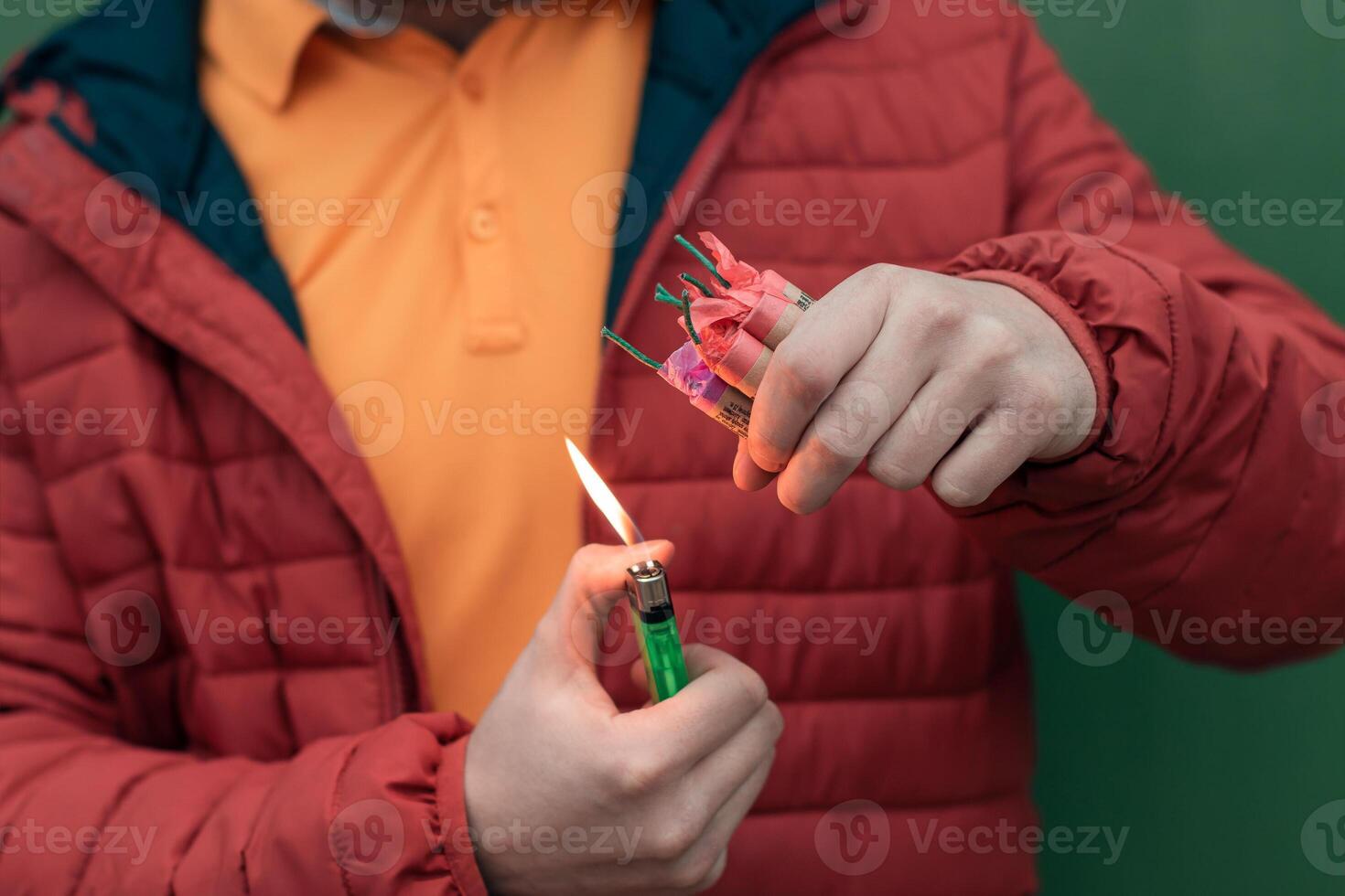 Man in Red Jacked Lighting Up Several Firecrackers in his Hand Using Gas Lighter. Guy Getting Ready for New Year Fun with Fireworks or Pyrotechnic Products photo