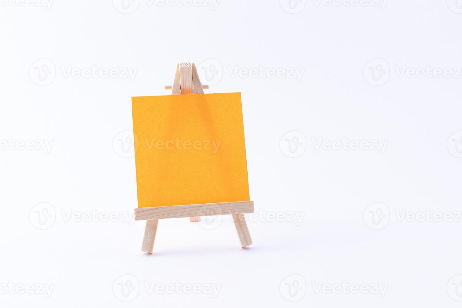 Wooden Easel Miniature with Blank Colored Square Canvas or Memo Paper - Mockup. Mini Wooden Stand with Clean Artboard on White Background, Copy Space photo
