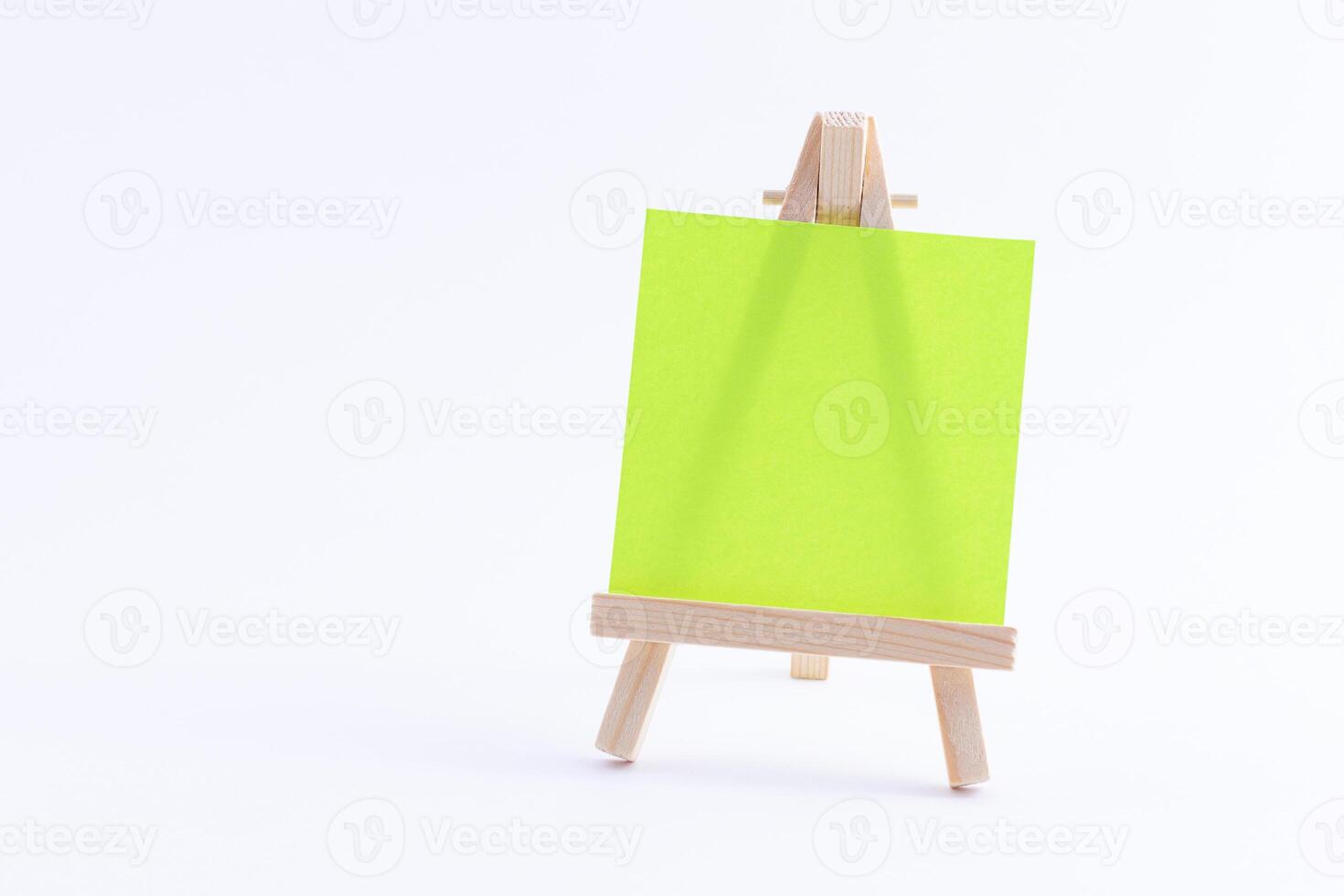 Wooden Easel Miniature with Blank Colored Square Canvas or Memo Paper - Mockup. Mini Wooden Stand with Clean Artboard on White Background, Copy Space photo