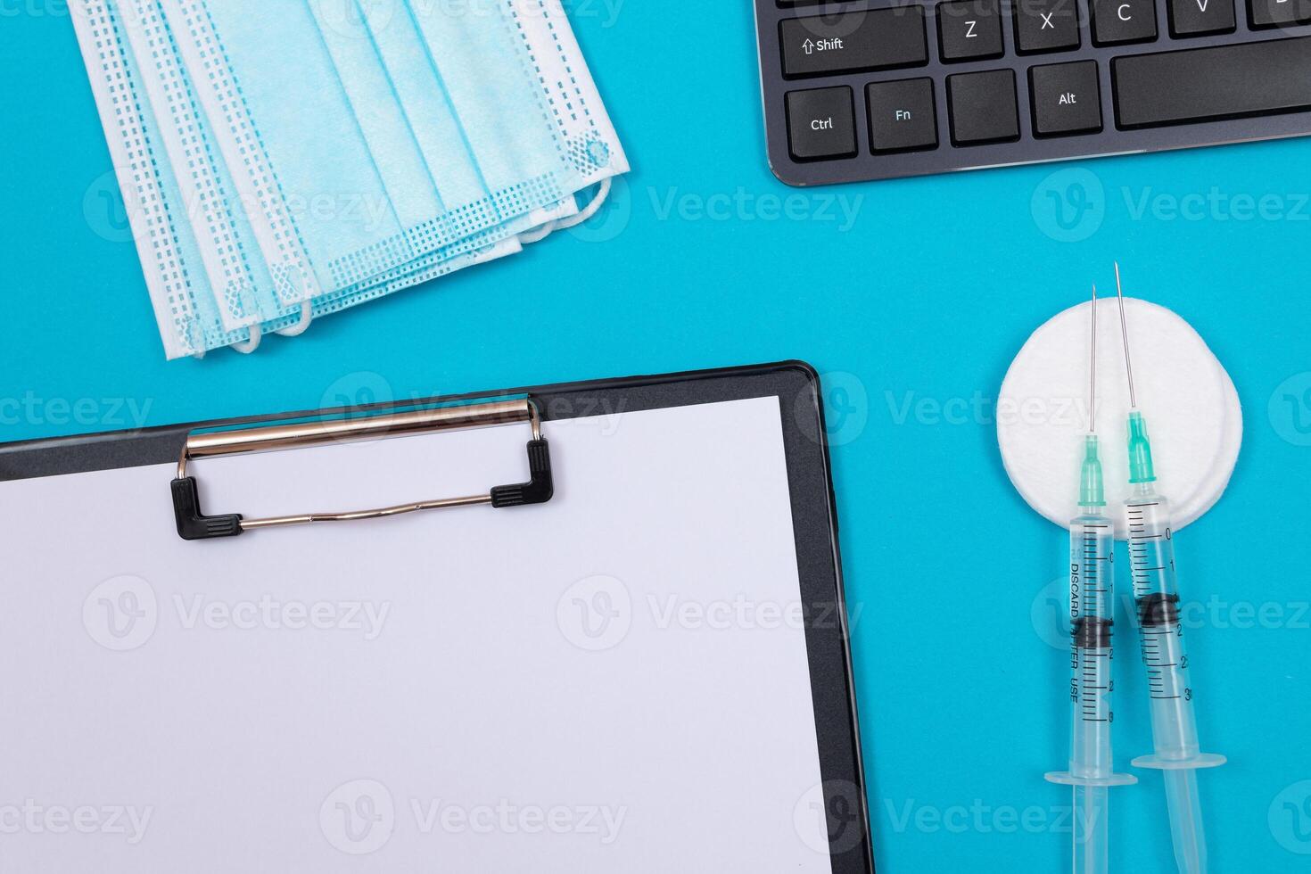 Vaccination, Immunology or Revaccination Concept - Two Medical Syringe Lying on Blue Table in Doctor's Office in a Hospital or Clinic. Black Clipboard with Sheet of Paper - Mock Up with Copy Space photo