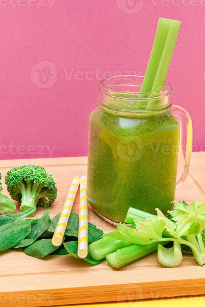 Fresh Green Smoothie of Apple, Celery, and Spinach in Glass Smoothie Jar with Yellow Cocktail Straw on Wooden Cutting Board. Vegan Detox Drink. Vegetarian Culture. Healthy Eating and Fruit Diet photo