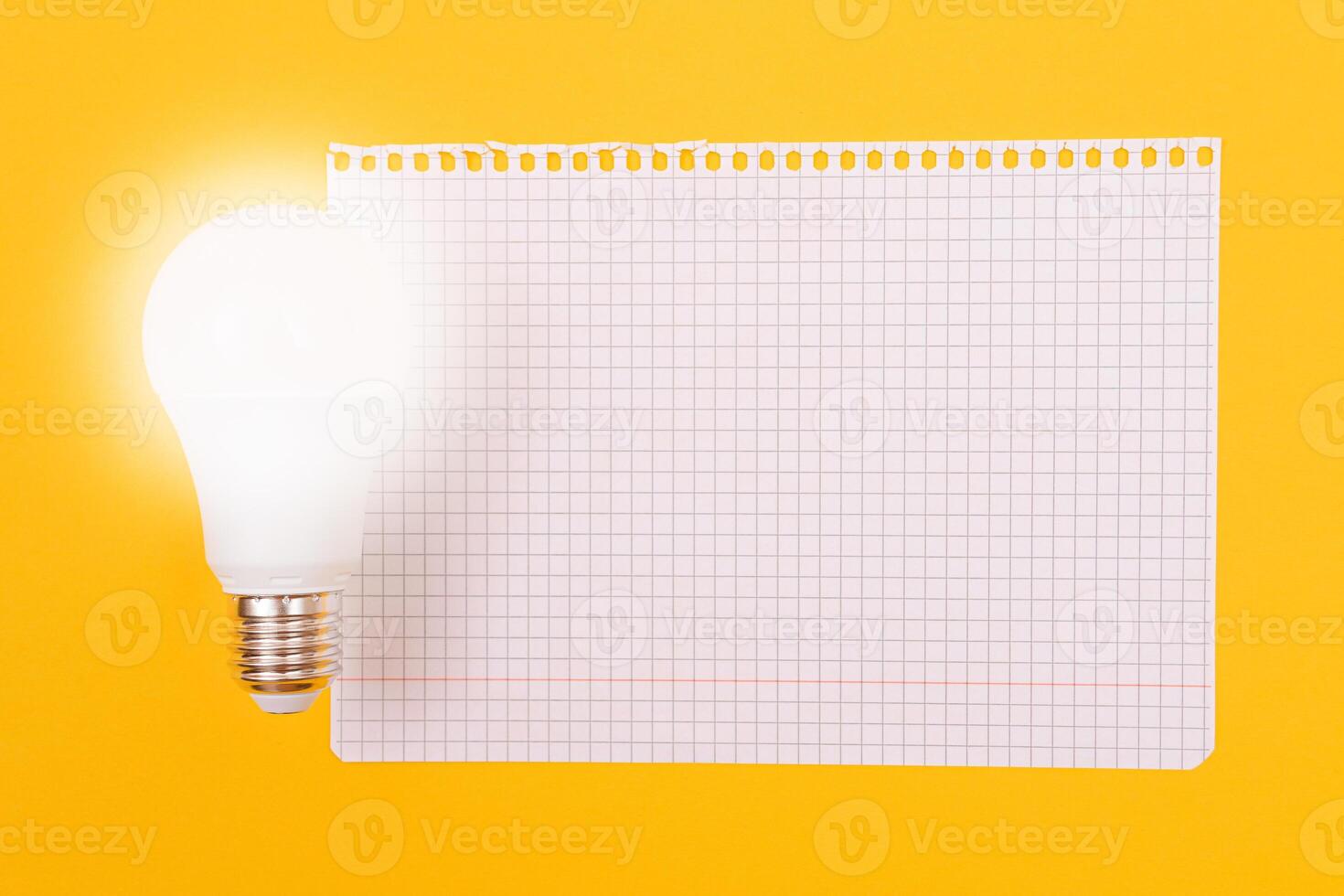 A Power Saving Lamp with Notepad Lying on Yellow Table, Blank Template with Copy Space - Top View, Flat Lay photo