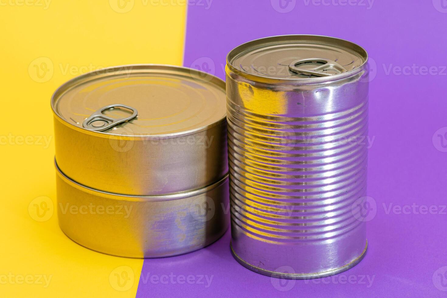 A Group of Stacked Tin Cans with Blank Edges on Split Yellow and Violet Background. Canned Food. Different Aluminum Cans for Safe and Long Term Storage of Food. Steel Sealed Food Storage Containers photo