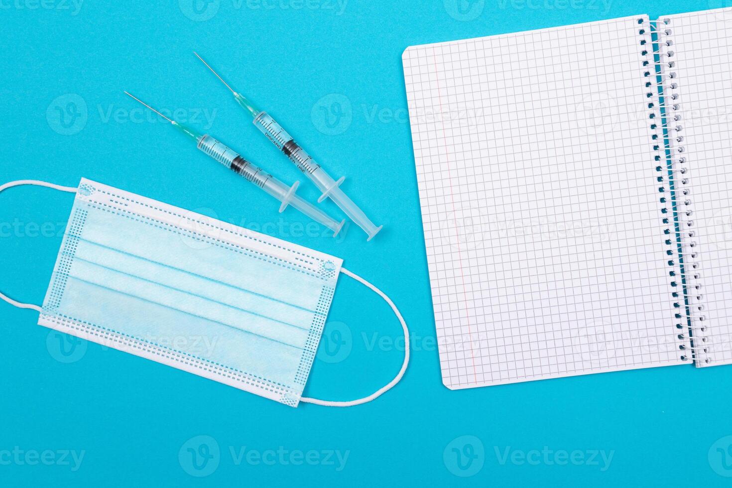 Vaccination, Immunology or Revaccination Concept - Two Medical Syringe Lying on Blue Table in Doctor's Office in a Hospital or Clinic. Opened Blank Notepad - Mock Up with Copy Space photo