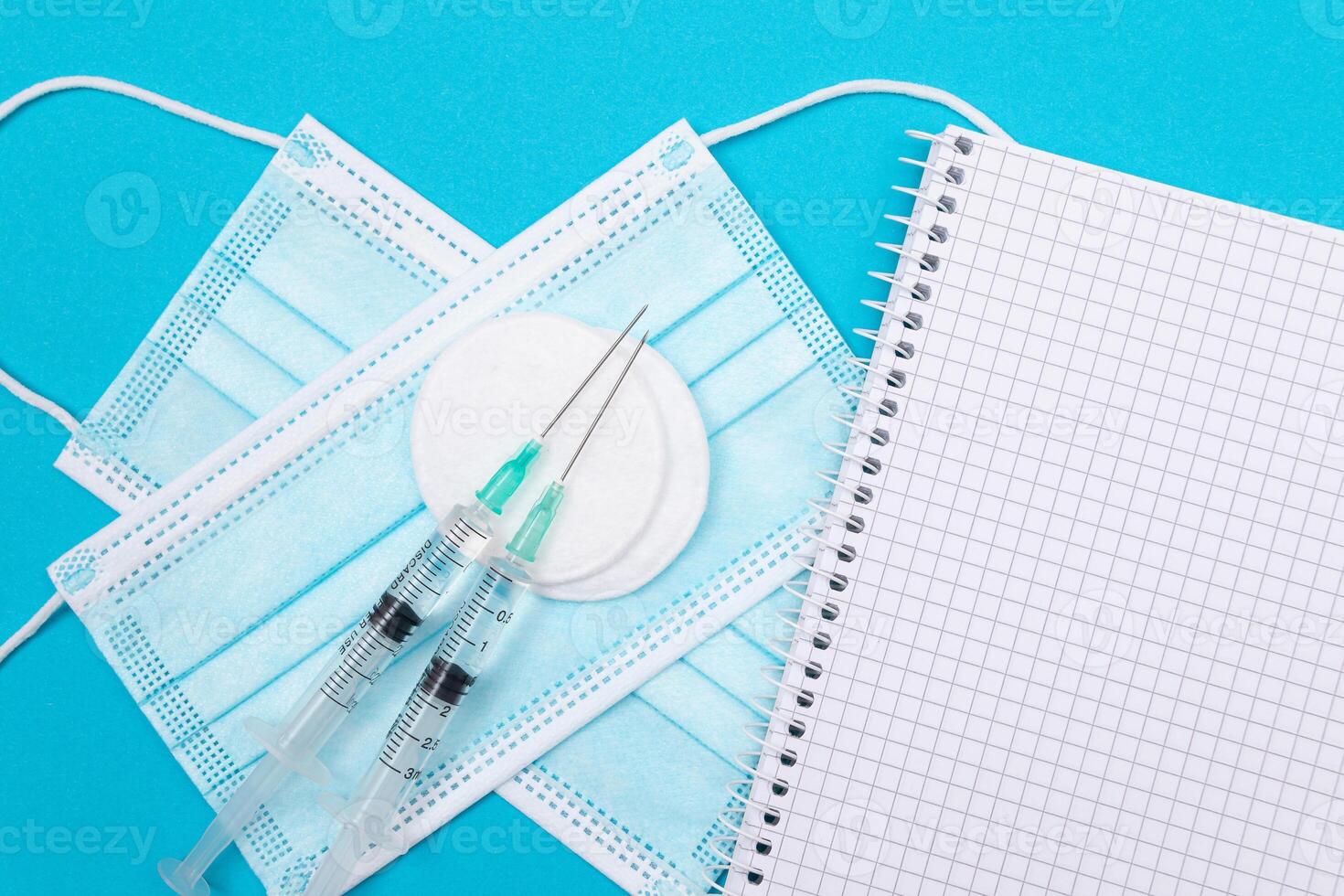 Vaccination, Immunology or Revaccination Concept - Two Medical Syringe Lying on Blue Table in Doctor's Office in a Hospital or Clinic. Opened Blank Notepad - Mock Up with Copy Space photo