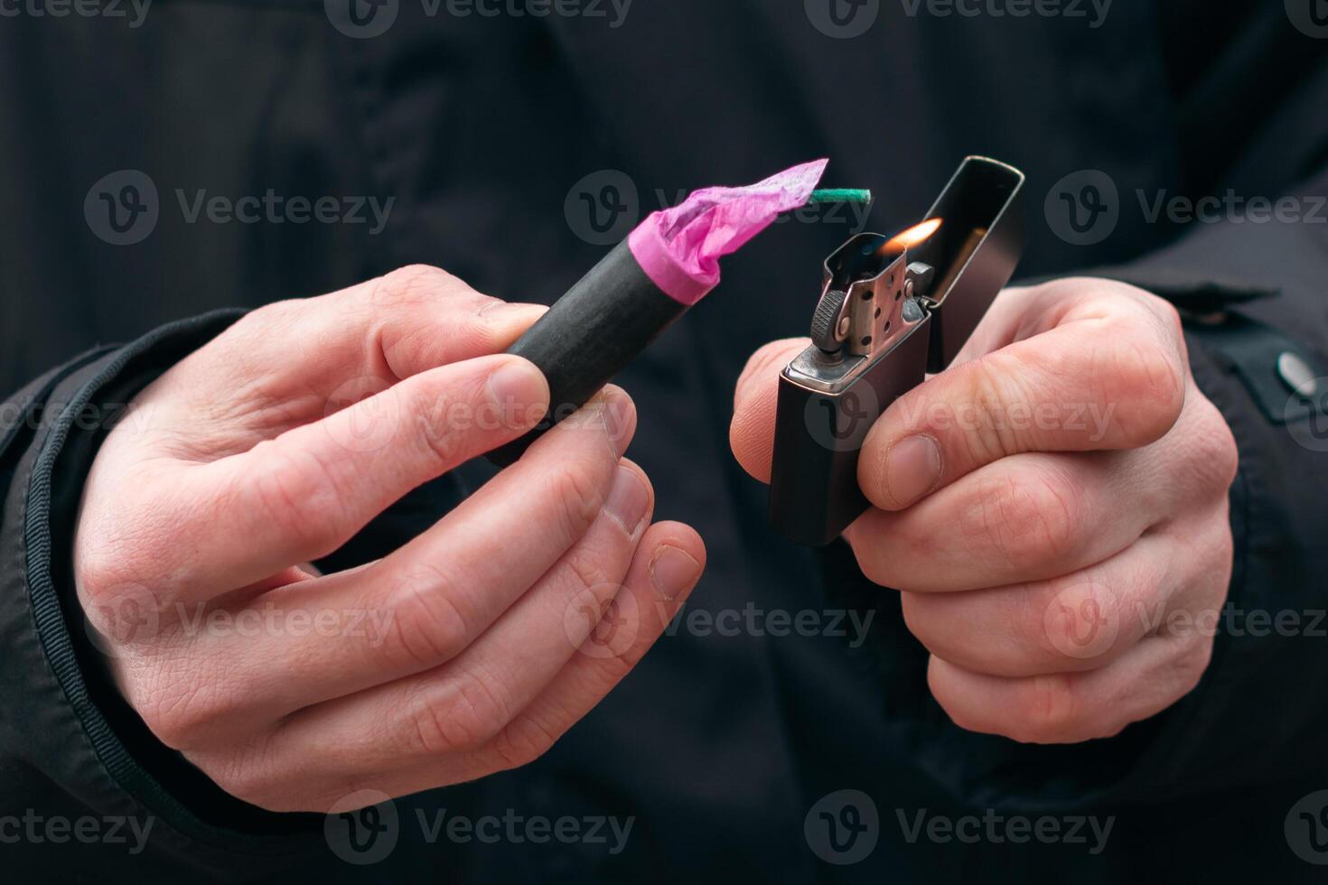 Setting Fire to the Firecracker. Man in Black Clothes Lighting Up the Petard. Firing Up the Pyrotechnics with a Black Gasoline Lighter Outdoors photo